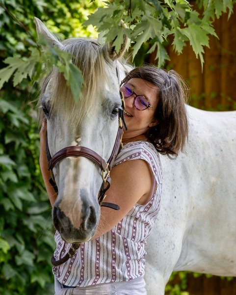 Muriel d'Hardemare-Lambert, fondatrice de MDHL Conseils, enlace un cheval blanc en souriant